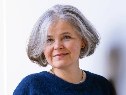 Julia Franck – Ältere Person mit grauen Haaren, blaue Strickpullover. Hintergrund weiß. Text: © Thorsten Greve.