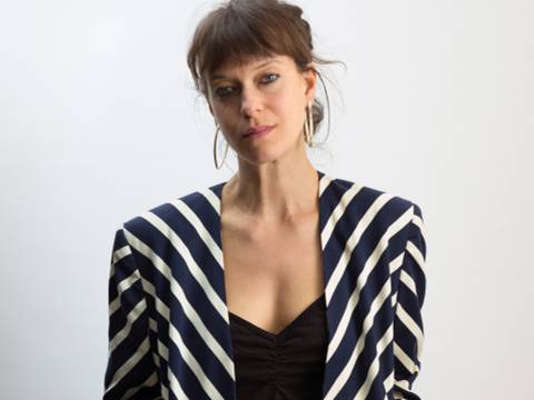 Katharina Bach – Halbporträt einer Person mit langen braunen Haaren im Zopf, trägt einen gestreiften Blazer.