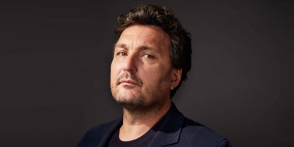 Ludovic Tézier – Ludovic Tézier mit dunklem lockigem Haar und dunklem Sakko blickt in die Kamera, neutraler Gesichtsausdruck, dunkler Hintergrund.