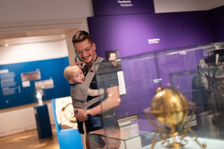 Besucher mit Baby im Museum Ephraim-Palais. – Ein Mann mit Baby im Tragetuch und einem Audioguide am Ohr in der Ausstellung BerlinZEIT