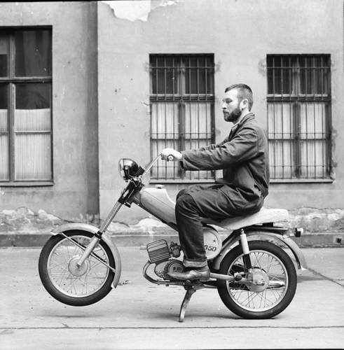Entwurfsmodell Mokick „Simson S 50“ im Hof des Ateliers von Lutz Rudolph am Helmholtzplatz, Prenzlauer Berg, Fotografie, um 1967 Gestaltung: Lutz Rudolph, Karl Clauss Dietel, Privatarchiv Ania Rudolph – Fotografie eines Mannes sitzend auf einem Motorrad-Modell in einem Berliner Hinterhof