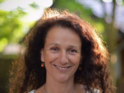 Anja Tuckermann – Eine lächelnde Person mit lockigem Haar trägt ein weißes Spitzenoberteil und eine silberne Halskette. Text: © Bernd Sahling.