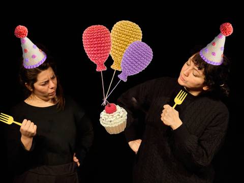 – Zwei Personen mit Partyhüten, halten Plastigabeln, betrachten einen gehäkelten Cupcake und Luftballons vor schwarzem Hintergrund.