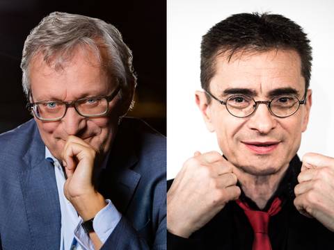  – Zwei Männer, links mit grauem Haar und Brille, rechte Hand am Kinn; rechts mit kurzem dunklem Haar, Brille, schwarzem Hemd und roter Krawatte, Fäuste gehoben.
