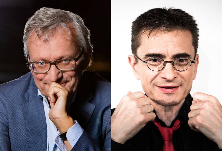 Zwei Männer, links mit grauem Haar und Brille, rechte Hand am Kinn; rechts mit kurzem dunklem Haar, Brille, schwarzem Hemd und roter Krawatte, Fäuste gehoben.