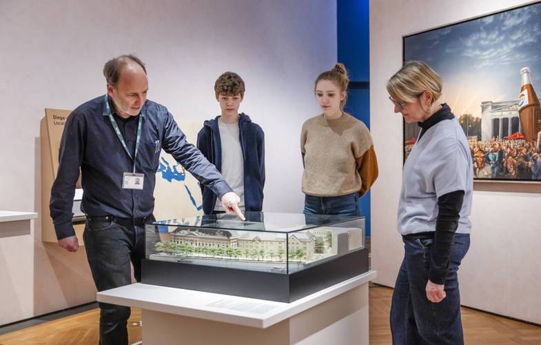 Ein Museumsführer steht vor einem Modell des Zeughauses und erklärt es drei Personen.
