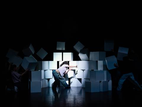 Das Ensemble der Jugendkompanie tanzhaus nrw, Düsseldorf mit "Flying High" – Performer*innen auf der Bühne, eine im Vordergrund durchbricht tanzend eine Mauer aus großen weißen Würfeln.