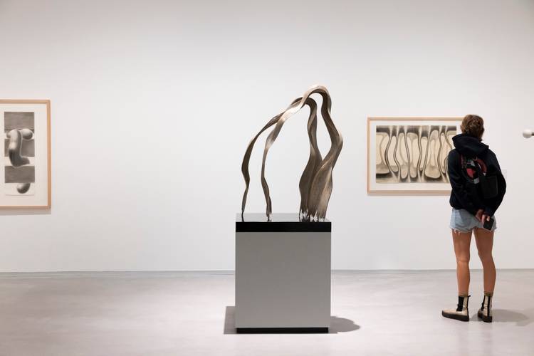 Ausstellungsansicht „Brigitte Meier-Denninghoff. Skulpturen und Zeichnungen 1946-1970“, Berlinische Galerie – Foto: Rückansicht einer Person, die vor einer Zeichnung und neben einer Skulptur von Brigitte Meier-Denninghoff im Ausstellungsraums steht.