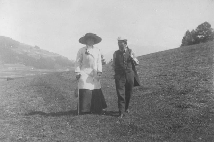 Auf der Erde: Alma und Gustav Mahler beim Spaziergang durch die Wiesen über Toblach im dunklen Sommer 1909 – Mann und Frau spazieren über Hügel
