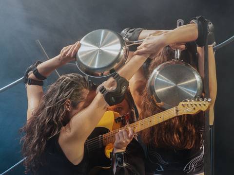 BANG! – Drei Personen auf einer Bühne, halten Kochtöpfe und Trommelstöcke. Eine Person spielt E-Gitarre. Bühnennebel im Hintergrund.
