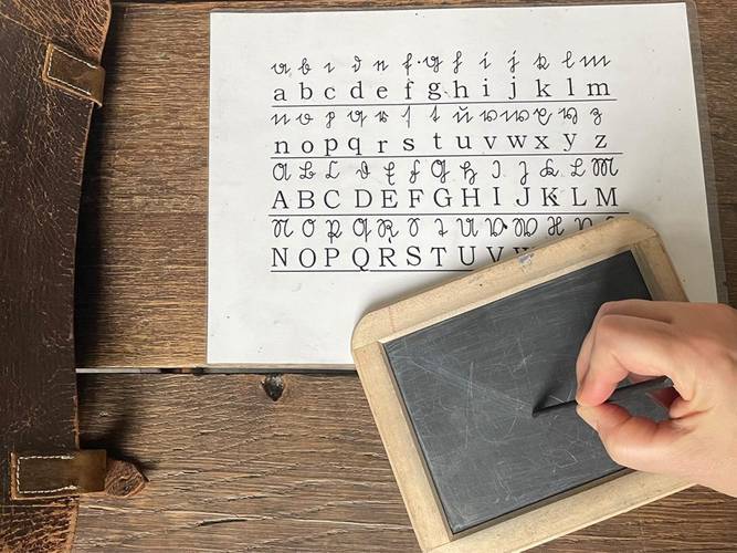 Um die Sütterlin-Schrift zu lernen, schrieben Kinder früher mit einem Griffel auf einer Schiefertafel. – Eine Person schreibt mit einem Griffel auf einer Schiefertafel