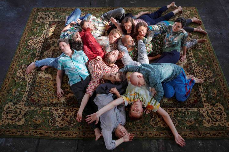Volker Heyn: TRANSFER 1 – Gruppenbild der Mitglieder des ensemble mosaik: alle Personen liegen über- und untereinander auf einem großen Teppich