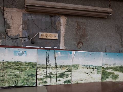  – Vier Fotografien einer Wüstenlandschaft stehen an einer alten, kaputten Wand.