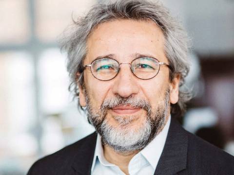  – Eine lächelnde Person mit grauen Haaren, Bart und Brille in einem dunklen Blazer, weißem Hemd vor unscharfem Hintergrund.