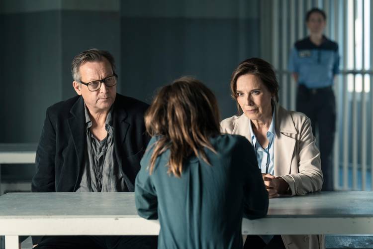 Matthias Brand und Désirée Nosbusch. © Stephan Rabold – Drei Leute sitzen an einem Tisch, hinter ihnen ein Polizeibeamter.