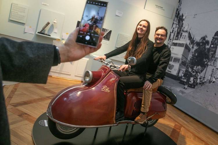 Der Motorroller „Pitty“ vermittelt beim Probesitzen einen sattelfesten Eindruck vom Berliner Straßenverkehr in den 1950er Jahren. – Zwei Besucher:innen beim "Foto-Shooting" auf dem Motorroller.