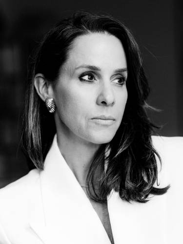 Natalie Amiri "Unsere Väter" – Person mit langen Haaren, ernster Blick zur Seite, trägt weißen Blazer und Ohrringe. Schwarz-Weiß-Fotografie.