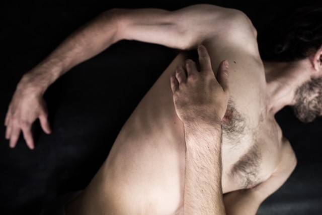 SAN PAOLO. Das Martyrium von Pasolini – Person liegt auf dem Rücken auf schwarzem Hintergrund, Körper größtenteils nackt, Hand auf Brust gelegt, Kopf außerhalb des Bildes.