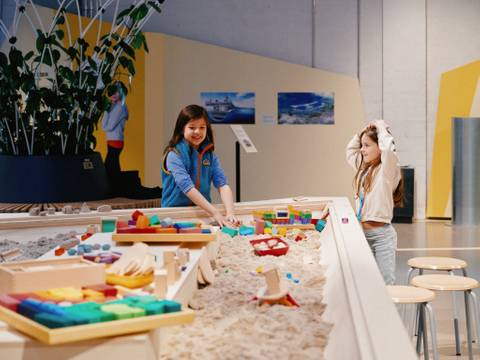 Mit kinetischem Sand und bunten Bauelementen können Kinder und Erwachsene selbstständig oder in Workshops an ihren Ideen für eine lebenswerte Stadt der Zukunft bauen. – Zwei Mädchen bauen in der Sonderausstellung "SuperCity 3000"