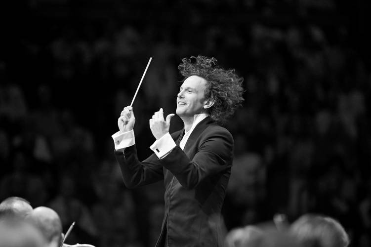 Nicholas Collon, Chefdirigent des Finnish Radio Symphony Orchestra – Ein Mann mit locken Haaren und einem Taktstock in der Hand dirigiert so überschwänglich, dass seine Haare herumwirbeln.