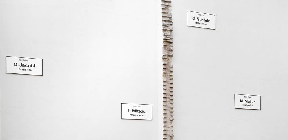Christian Boltanski, The Missing House, Detail, 1990/2025, Rekonstruktion der ortsspezifischen Installation, 24 Schilder auf zwei Brandmauern, 2025 Schenkung von Annette Messager. Courtesy Fonds de dotation Christian Boltanski – Weiße Wand mit vier Namensschildern: G. Jacobi Kaufmann, G. Seefeld Holzkaufmann, L. Miteau Verwalterin, M. Müller Pensionärin.