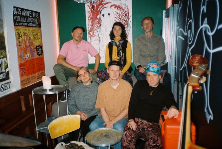 Ingebrigt Håker Flaten (Exit) Knarr – Eine Gruppe von Personen in einem Raum mit Postern und Kunst an der Wand, sitzend und stehend. Instrumenten nah.