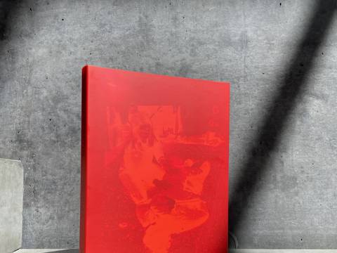 „Özlem Altın. Prisma“, Ausstellungskatalog, Distanz Verlag 2024 – Foto: Ein aufgestellter Ausstellungskatalog steht aufrecht vor einer grauen Betonwand im Sonnenlicht.