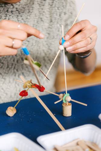 Foto: Nahaufnahme von zwei Händen, die eine Art Mobile aus verschiedenen Materialien wie Kork, Holz und Papier in halten.