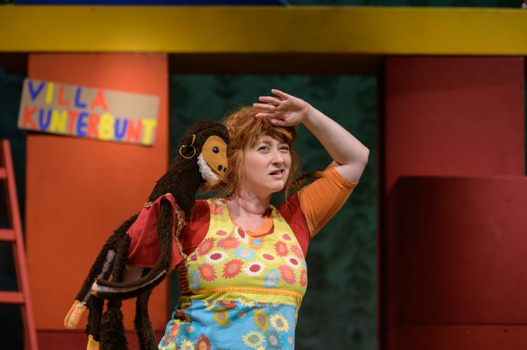 Pippi Langstrumpf – Person mit bunter Kleidung hält einen Affen-Puppe, im Hintergrund ein Schild mit "VILLA KUNTERBUNT".