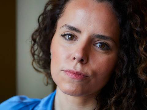  – Person mit lockigem Haar und blauem Hemd schaut in die Kamera. Hintergrund unscharf.