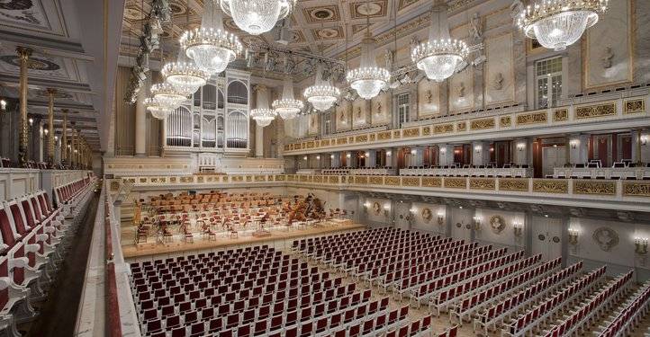Großer Konzertsaal mit roten Sitzreihen, Orchesterbühne mit Instrumenten, prächtige Kronleuchter an der Decke, Orgel im Hintergrund, Balkon mit mehr