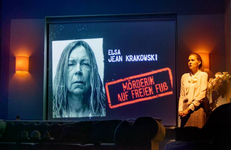 Ist sie das wirklich? Vonl li.: Marion Kracht und Jessica Ginkel. – Projektionswand mit Text "Elsa Jean Krakowski" und "Moerderin auf freiem Fuss", daneben eine stehende person mit heller Bluse vor einer Wandlampe.