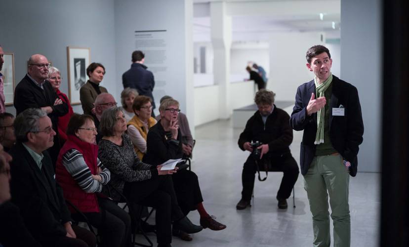 Zirkeltraining in der Berlinischen Galerie – Foto: Viele Menschen stehen und sitzen im Ausstellungsraum und schauen auf eine Person, die spricht und auf ein Gemälde deutet.