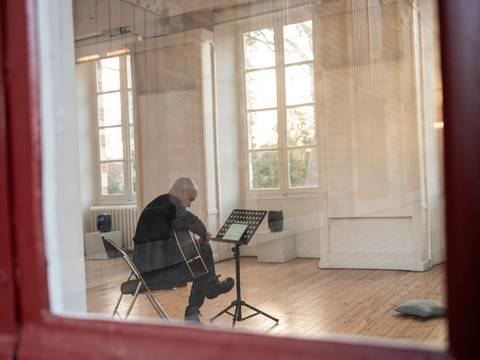 Didier Aschour spielt point/wave von Catherine Lamb – Ein Mann mit Gitarre sitzt in einem Raum mit vielen Fenstern im Sonnenlicht.