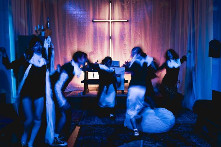 Foto: Michał Wojtarowicz – Fünf Personen in Bewegung vor einem blau beleuchteten Raum mit großem leuchtendem Kreuz an der Wand.
