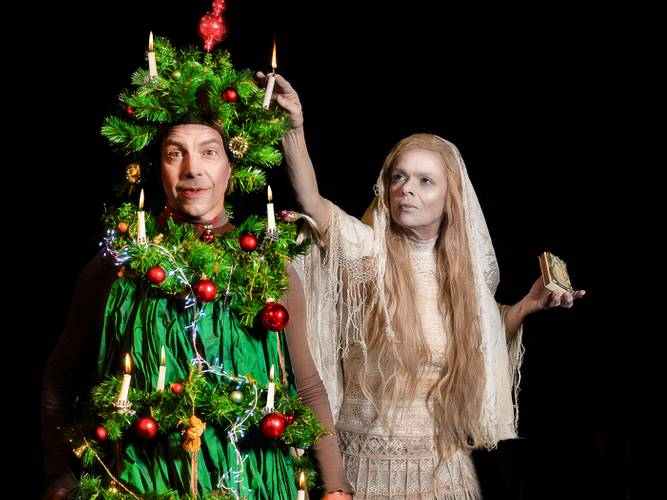 Märchen im Glaspalast von und mit dem Hexenberg Ensemble: Der Tannenbaum | Das Mädchen mit den Schwefelhölzern – Eine Person in Weihnachtsbaumkostüm mit Kerzen und Kugeln; daneben eine langhaarige Person in weißem Kleid mit Kerze.