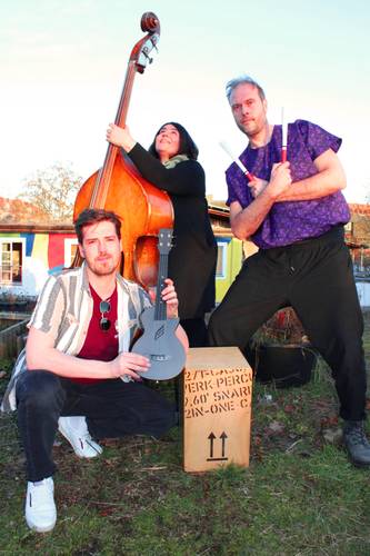 Drei Personen mit Instrumenten: eine*r mit Kontrabass, eine*r mit Schlägeln neben einer Kiste, auf der "2in-One-Cajon" steht, und eine*r mit einer E-Gitarre.