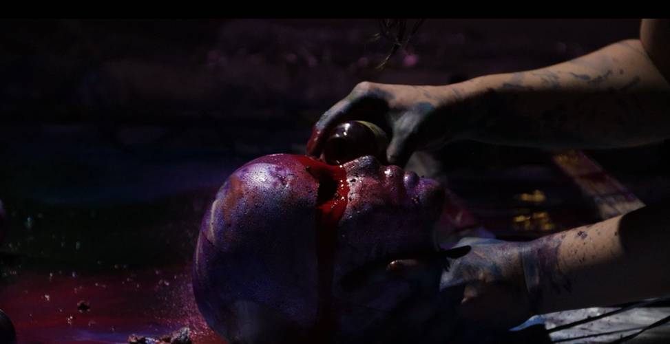 Verfärbter menschlicher Kopf mit roter Flüssigkeit. Hände mit farbigem Fleck bedeckt, halten dunklen Gegenstand darüber. Dunkle und violette Umgebung.