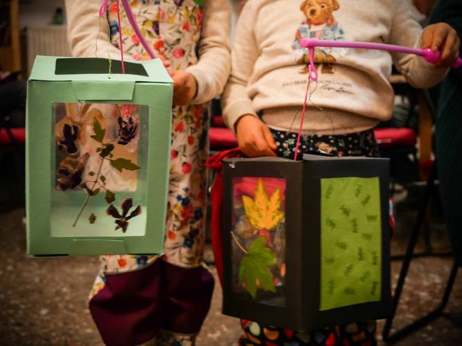 Zwei Kinder halten bunte Papierlaternen mit gepressten Blättern und Blüten. Eine Laterne ist grün, die andere schwarz mit grünem Dekor.