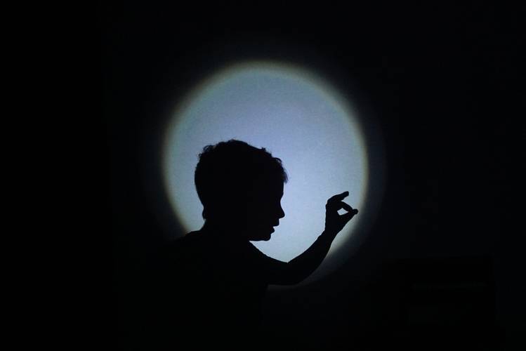 Schattenwerfer – Eine Person wirft einen Schattensilhouette auf eine Wand, die Person formt mit der Hand einen Kreis in Richtung des Lichts.