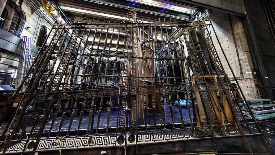 Backstage-Führung – Großes verziertes Metallgitter in einem Theaterbühnenbereich, umgeben von technischen Ausrüstungen und gerahmt von industriellen Baustrahlern.