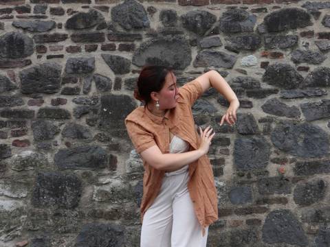 Heimat. Suchend. – Eine junge Frau vollführt eine tänzerische Bewegung vor einer Steinwand.