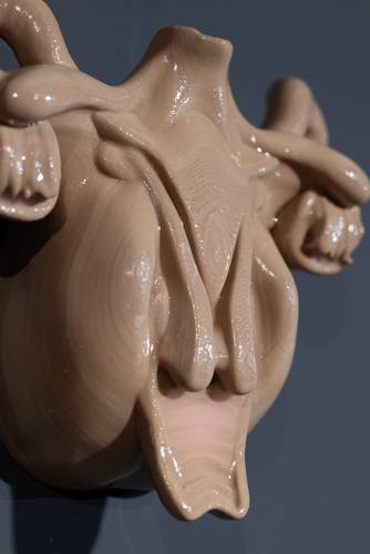 Beige skulpturale Form mit glatten, wellenförmigen Linien und glänzender Oberfläche auf dunkelgrauem Hintergrund.