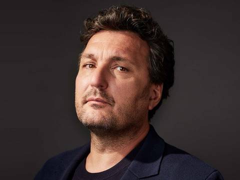 Ludovic Tézier – Ludovic Tézier mit dunklem lockigem Haar und dunklem Sakko blickt in die Kamera, neutraler Gesichtsausdruck, dunkler Hintergrund.