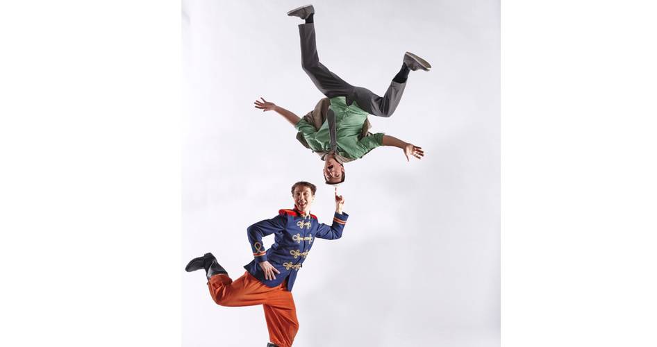 Kinder- und Familientheater Coq Au Vin: Der Dieb im Zirkus – Zwei Personen in akrobatischer Pose: Eine Person steht auf einem Bein, die andere schwebt kopfüber, beide in bunten Kostümen.