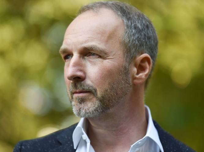 Stefan Schwarz: Oops – eine Weltgeschichte des Unerwarteten – Person mit kurzem Haar und Bart schaut nach links, trägt ein weißes Hemd und dunkles Jackett. Unscharfer, gelb-grüner Hintergrund.