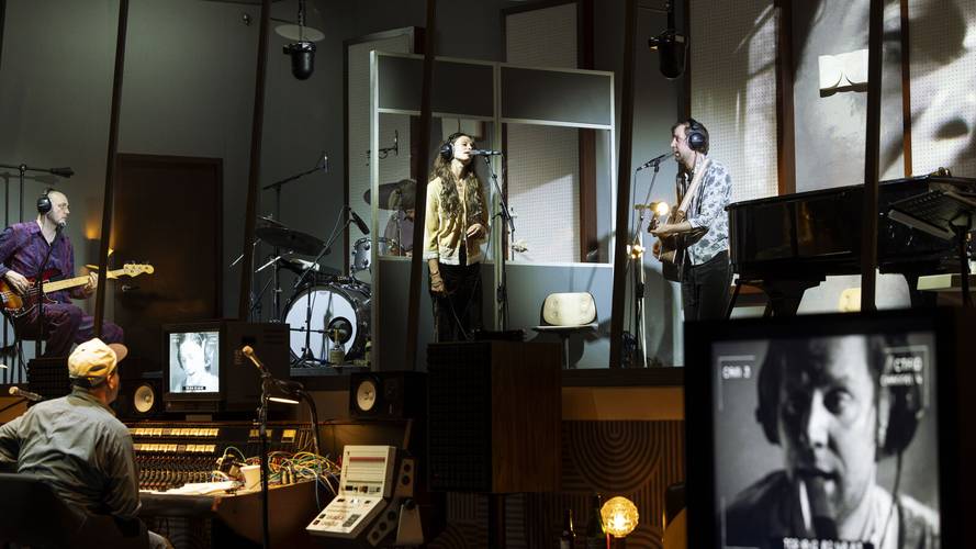 Stereophonic – Vier Personen mit Kopfhörern in einem Studio. Zwei singen in Mikrofone. Bildschirme mit Nahaufnahme eines rauchenden Sängers. Mischpult im Vordergrund.