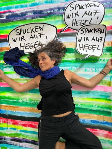 Person mit blauem Schal vor buntem Hintergrund, Sprechblasen: "SPUCKEN WIR AUF HEGEL!"