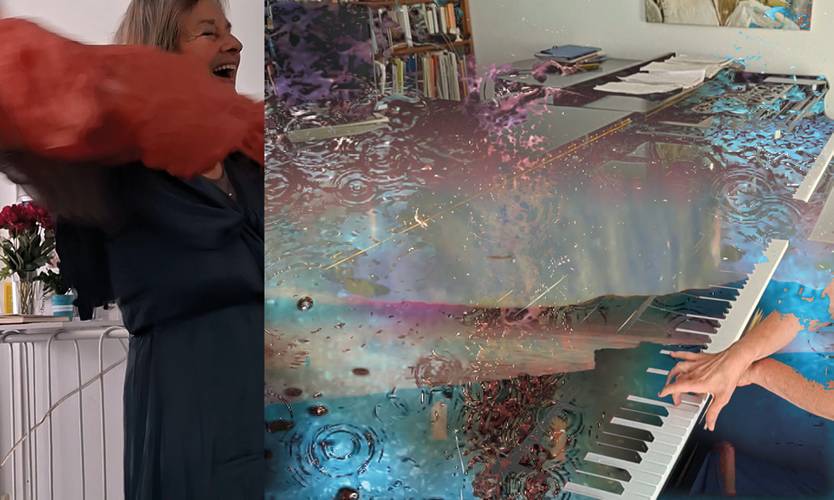 Person in blauem Kleid hebt orange Stoff; daneben Hände auf Klavier mit buntem, wasserartigem Effekt; im Hintergrund Bücherregal und Kunst.