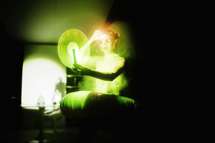 Soft Squishy Things – Eine Person mit nacktem Oberkoerper haelt einen leuchtenden Ring und Stab vor dunklem Hintergrund, mit gruenem Nebel und Licht.
